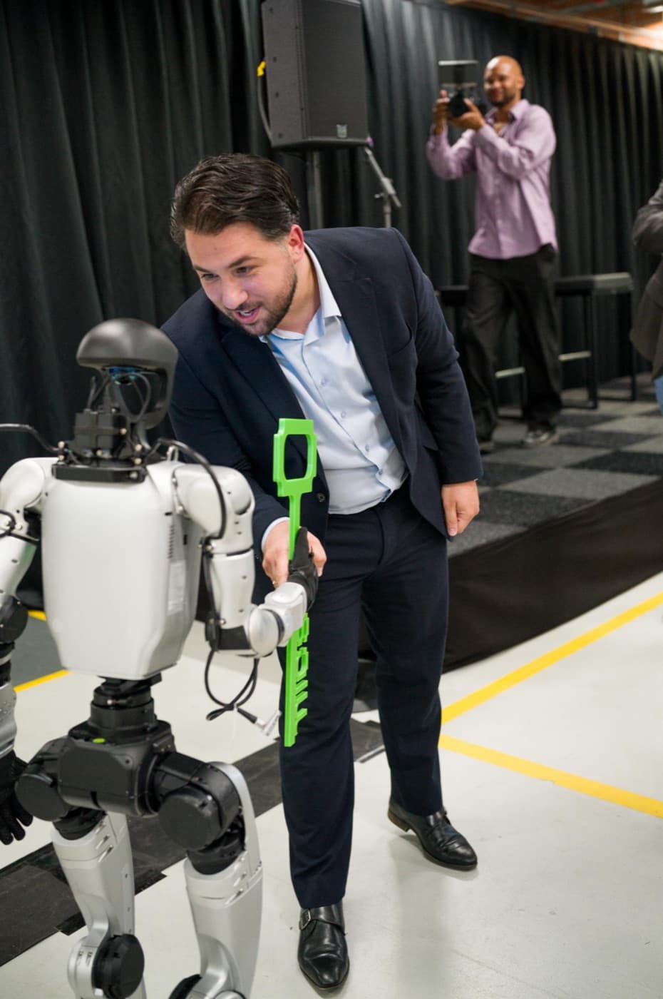 Wethouder oog in oog met een humanoid, wisselt de groene MICS-sleutel uit op de openingsvloer